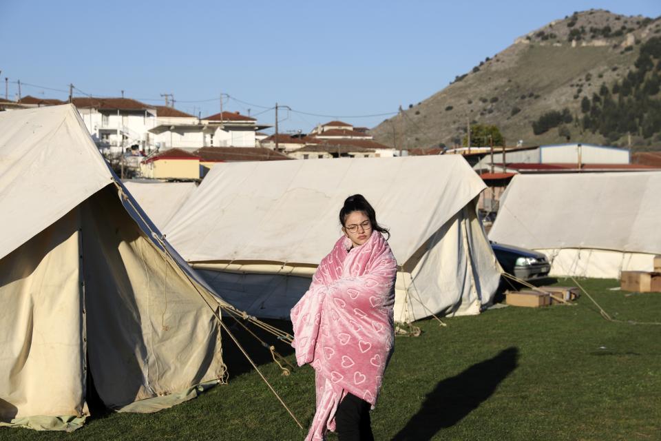 A girl standing outside a tent, uses a blanket to stay warm after an earthquake in Damasi village, central Greece, Thursday, March 4, 2021. Fearful of returning to their homes, thousands of people in central Greece spent the night outdoors after a powerful earthquake, felt across the region, damaged homes and public buildings. (AP Photo/Vaggelis Kousioras)
