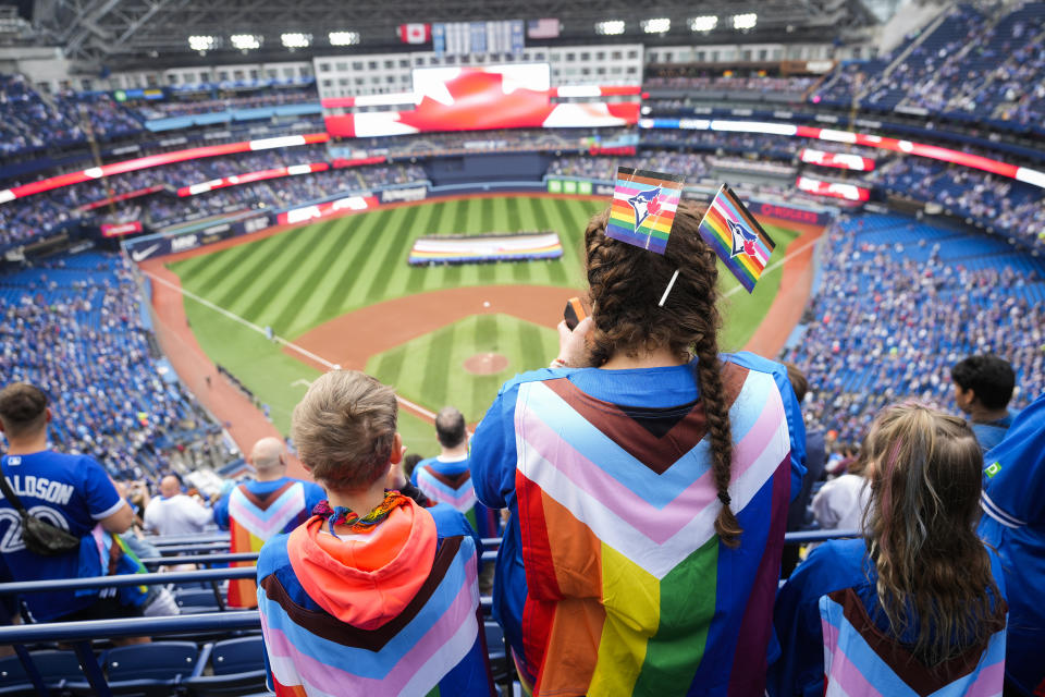 Fans wearing Pride-themed flags stand during the national anthems before a baseball game between the Toronto Blue Jays and the Minnesota Twins, Friday, June 9, 2023, in Toronto. (Mark Blinch/The Canadian Press via AP)