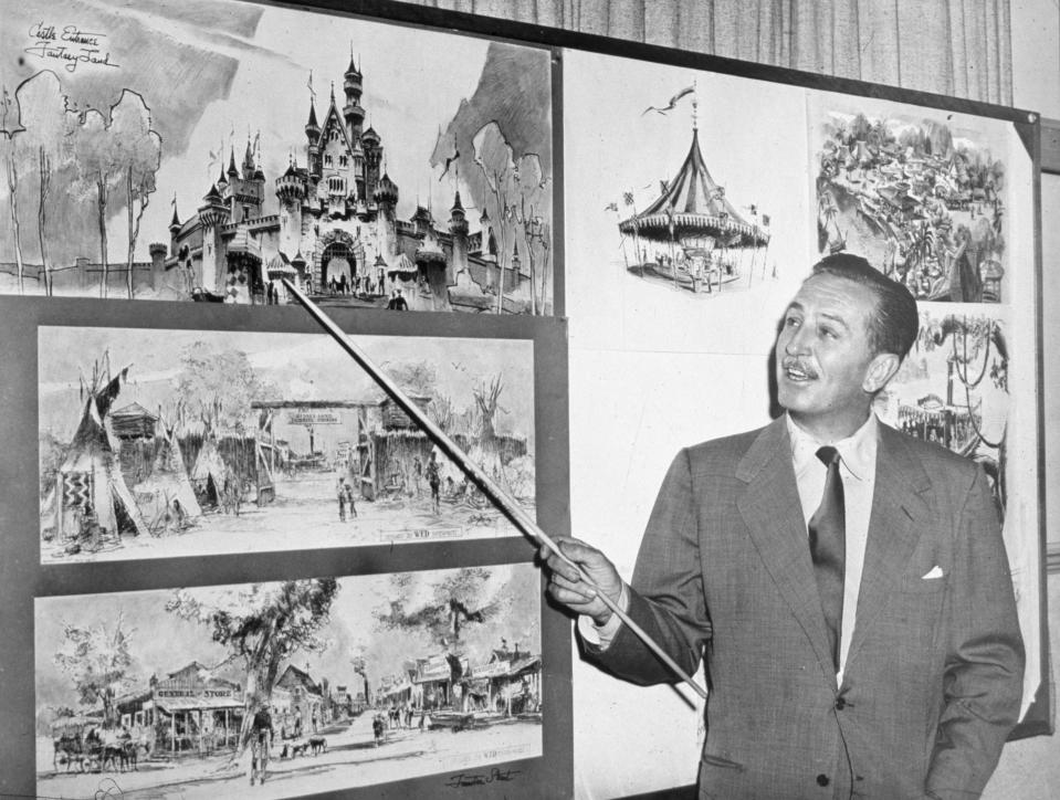 Walt Disney uses a baton to point to sketches of Disneyland