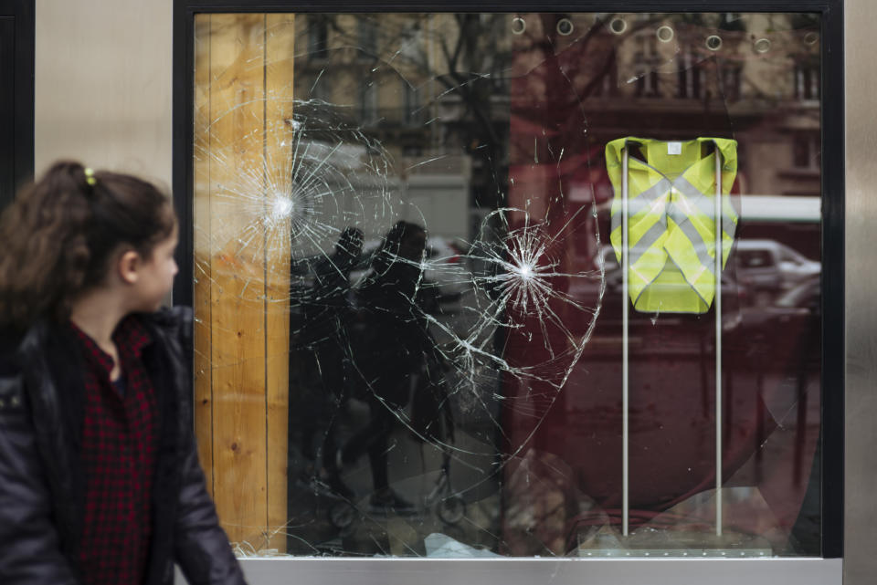 A woman passes a smashed window displaying a yellow vest, showing support for protesters and for protesters not to attack the building, near the Arc de Triomphe, in Paris, Sunday, Dec. 2, 2018. A protest against rising taxes and the high cost of living turned into a riot in the French capital Saturday, as activists caused widespread damage and tagged the Arc de Triomphe with multi-colored graffiti during clashes with police. (AP Photo/Kamil Zihnioglu)