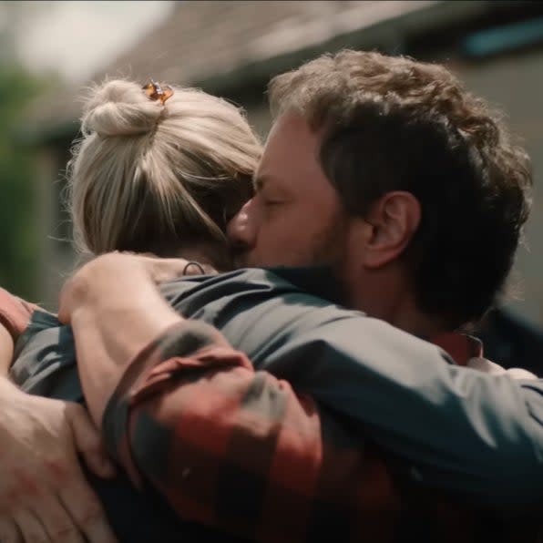 Two people embracing outdoors, with one person's back to the camera and the other kissing their cheek