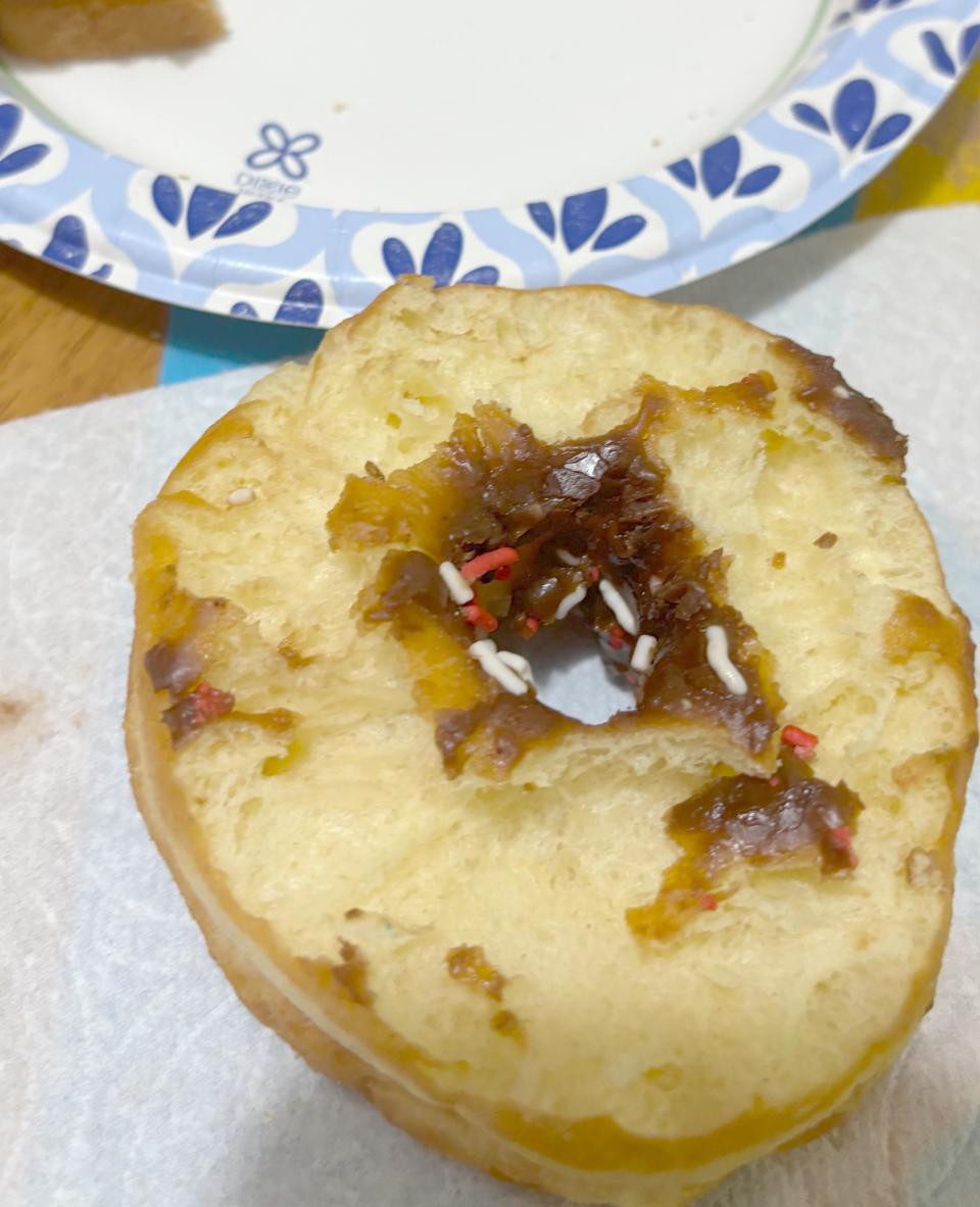 A donut with a hole filled with caramelized sauce and sprinkles on a paper plate