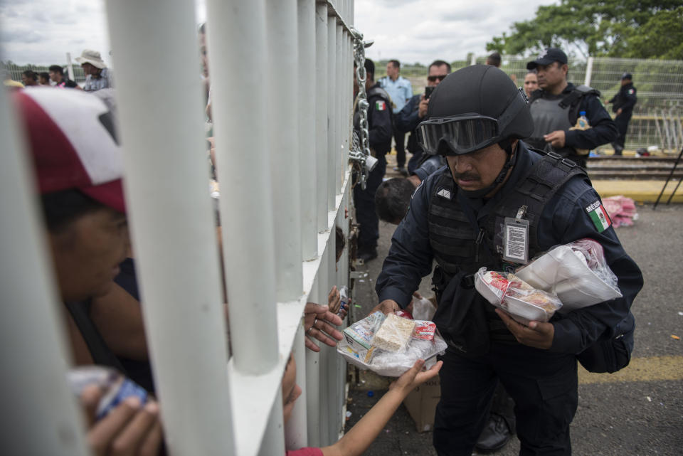 A Mexican Federal Police officer hands out food to Honduran migrants stuck in no man's land on the bridge over the Suchiate River that is the border between Guatemala and Mexico, near Ciudad Hidalgo, Mexico, Saturday, Oct. 20, 2018. The entry into Mexico via the bridge has been closed. The migrants have moved about 30 feet back from the gate that separates them from Mexican police to establish a buffer zone. About 1,000 migrants now remain on the bridge between Guatemala and Mexico. (AP Photo/Oliver de Ros)