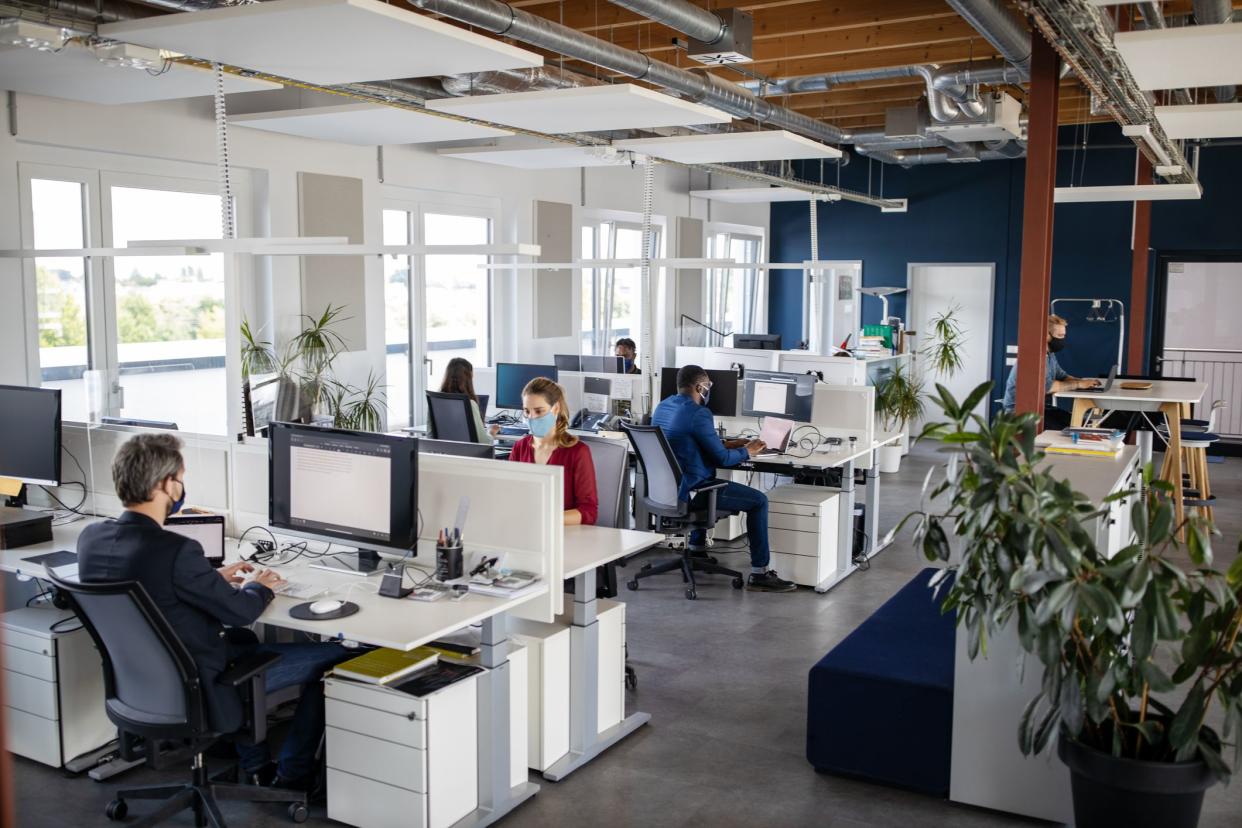 Business people with face masks sitting at their desks and working on computers. People working in an open plan office during pandemic.