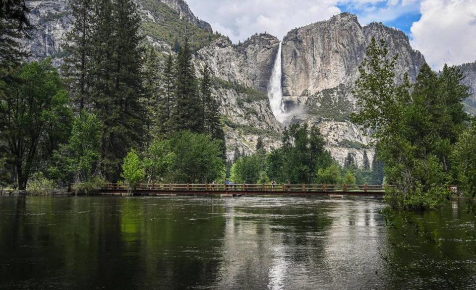 The bridge at the Swinging Bridge picnic area in Yosemite Valley sits just above the water level of the Merced River as Upper Yosemite Falls flows in the background on Tuesday, June 14, 2023.