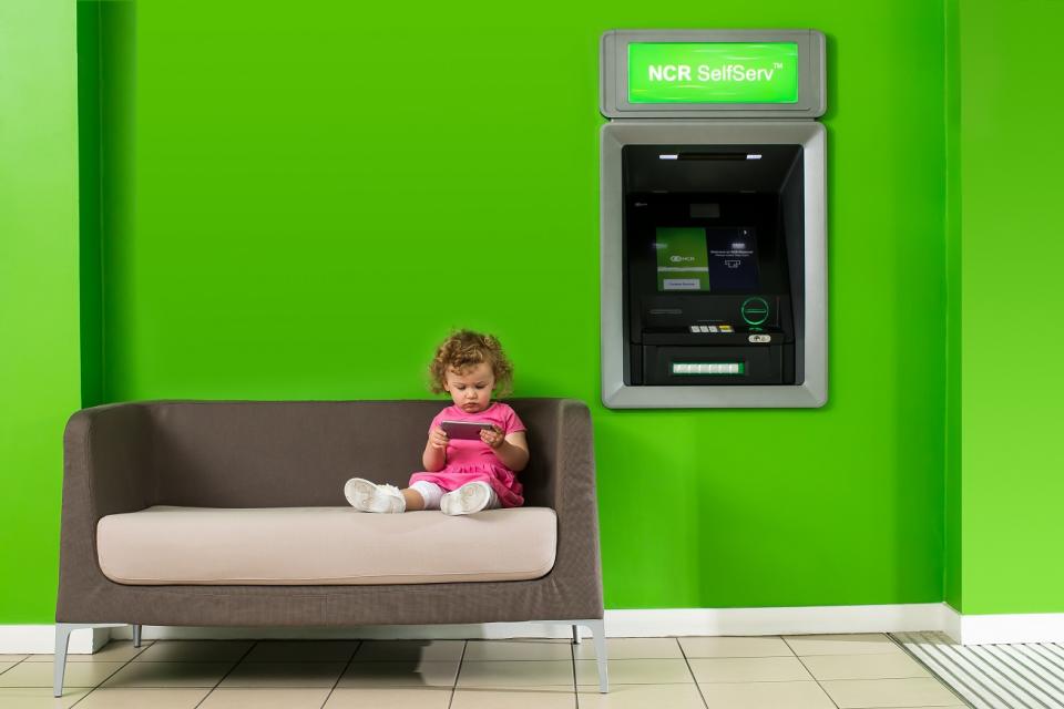 Child sitting on a couch in front of an NCR ATM.