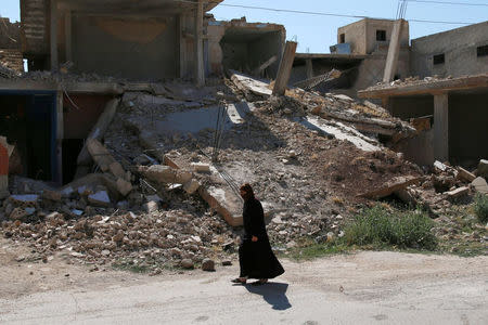 A woman walks past damaged buildings along a street in the rebel-held town of Dael, in Deraa Governorate, Syria July 7, 2016. REUTERS/Alaa Al-Faqir