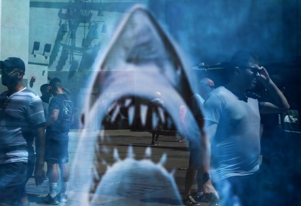 People walk past a Jaws poster reflected in a mirror.