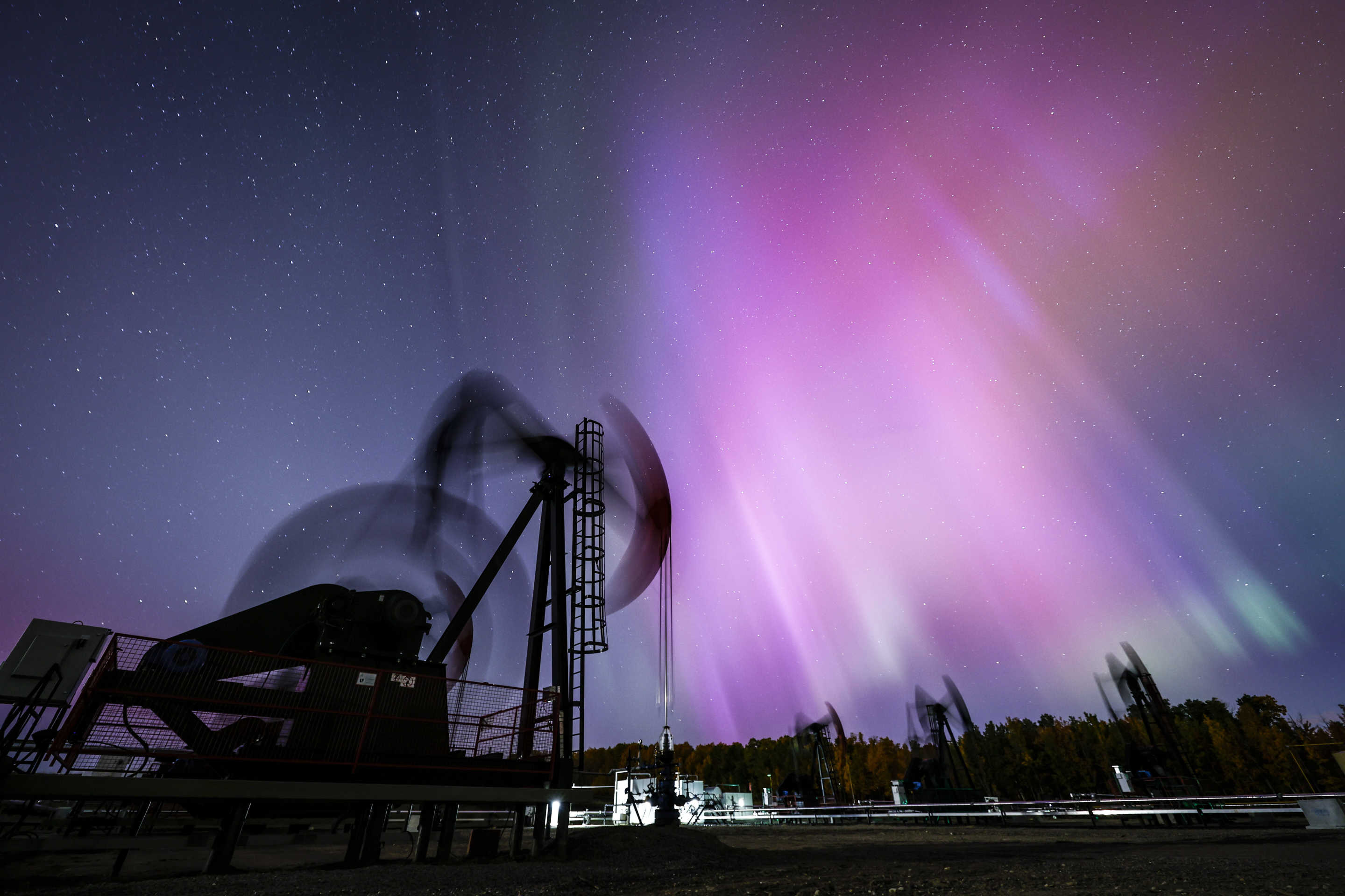 Aurora borealis against silhouette of oil pumping machinery.