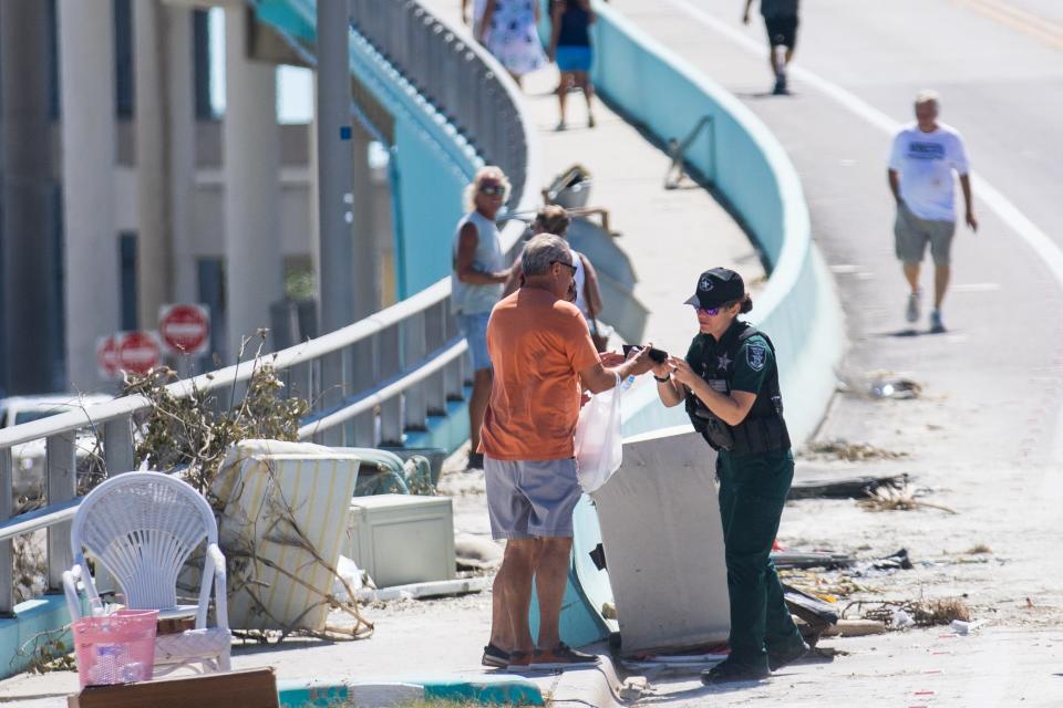 A Lee County Sheriff's Deputy checks IDs of pedestrians crossing the bridge over Matanzas Harbor after Hurricane Ian passed through the region Wednesday afternoon in Fort Myers, FL., on Friday, September 30, 2022. On Friday afternoon the bridge was open to residents of Fort Myers Beach so they could cross and retrieve their belongings from homes that were destroyed by Hurricane Ian.