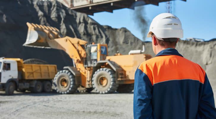 a construction worker looks on as an excavator gets to work in a mine. Mining Stocks