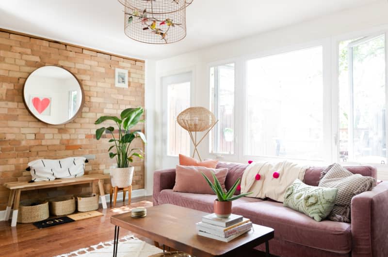 Living room with pink sofa, midcentury coffee table, exposed brick wall, and round mirror