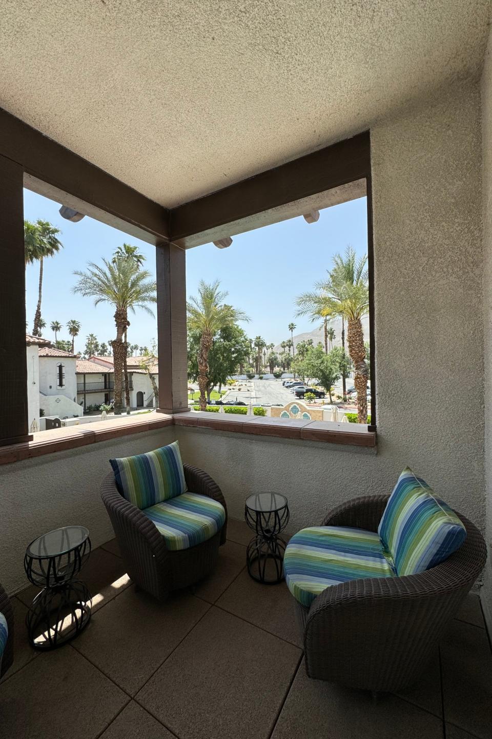 View from a covered patio with casual seating overlooking a sunny street lined with palm trees