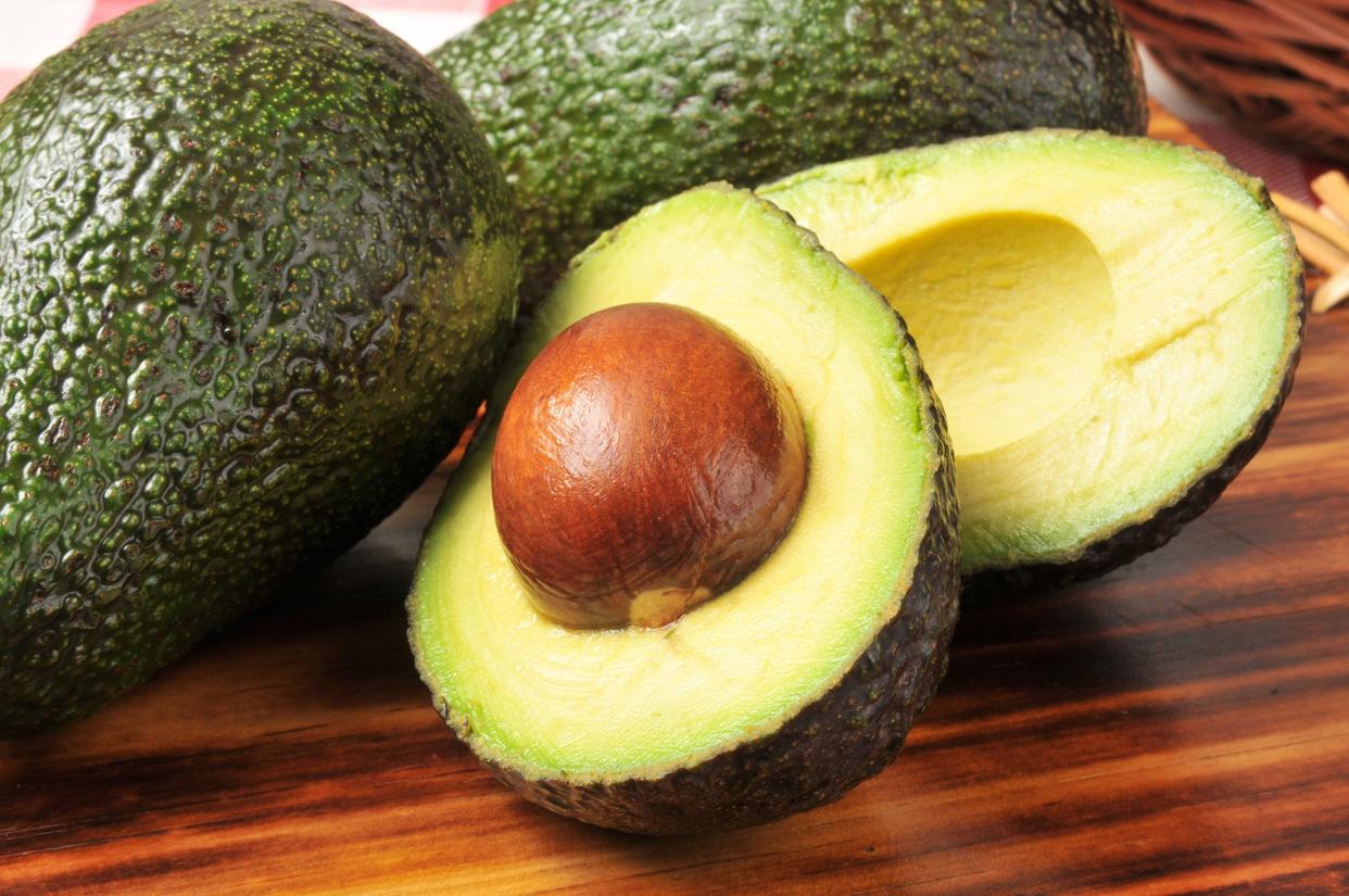 sliced avocado showing pit with two other avocados