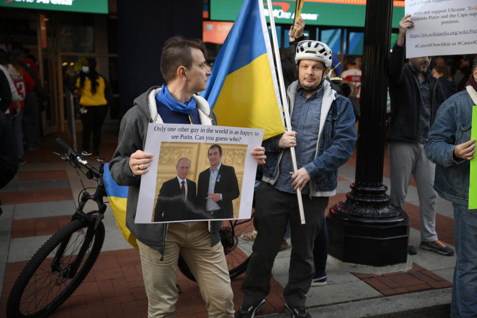 Demonstrators display a picture showing Vladimir Putin and Washington Capitals' Alex Ovechkin as well as Ukrainian flags outside of the entrance of Capital One Arena before an NHL hockey game between the Washington Capitals and the Seattle Kraken, Saturday, March 5, 2022, in Washington. (AP Photo/Nick Wass)
