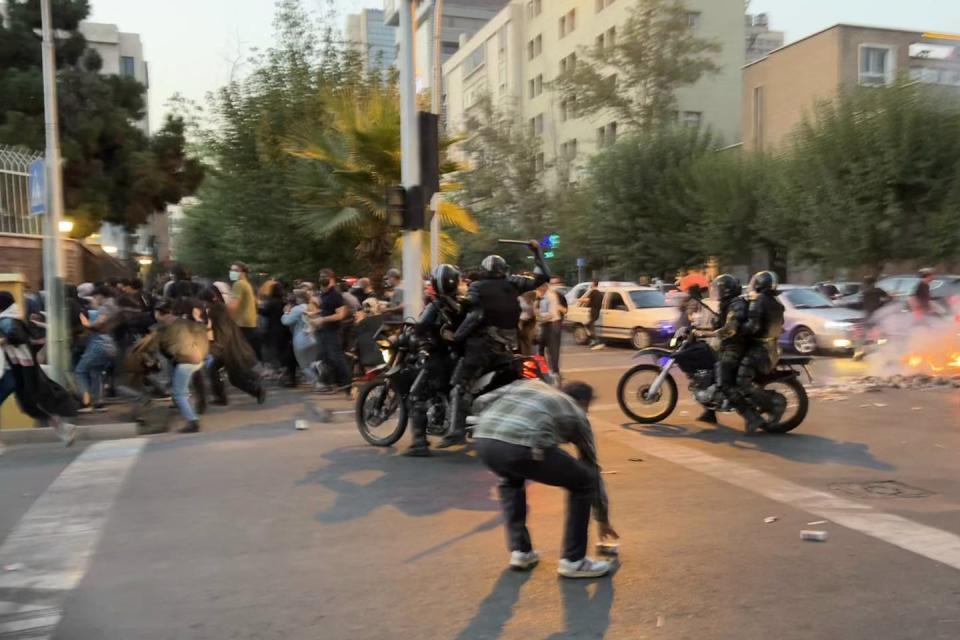 Police on motorbikes weild a baton while a group of protestors scatter.