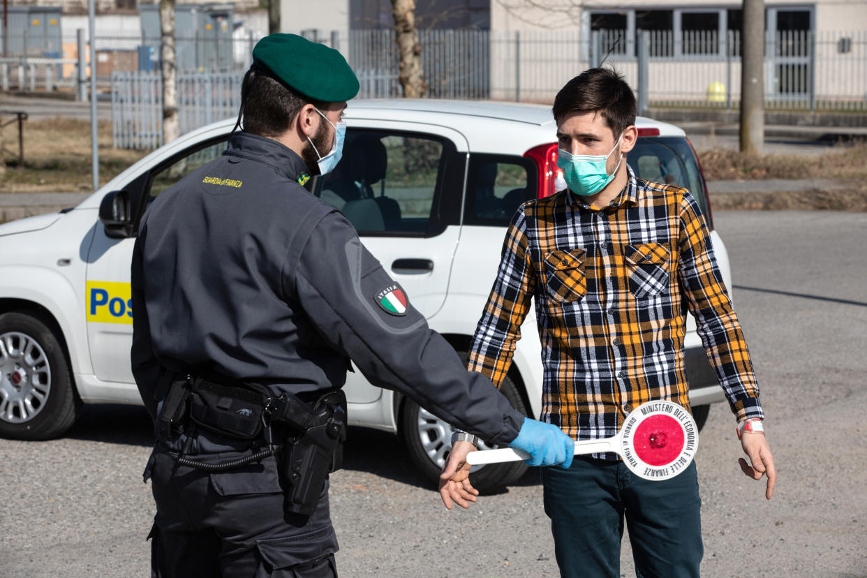 CASALPUSTERLENGO, ITALY - FEBRUARY 24: An Italian Guardia di Finanza (Custom Police) officer, wearing a respiratory mask, talks to a young man at a road block on February 24, 2020 in Casalpusterlengo, south-west Milan, Italy. Casalpusterlengo is one of the ten small towns placed under lockdown after coronavirus sparked infections throughout the Lombardy region. Italy is the last country to be hit hard by the virus with five dead and more than 224 infected as of today. The spread marks Europe’s biggest outbreak, prompting Italian Government to issue draconian safety measures. (Photo by Emanuele Cremaschi/Getty Images)