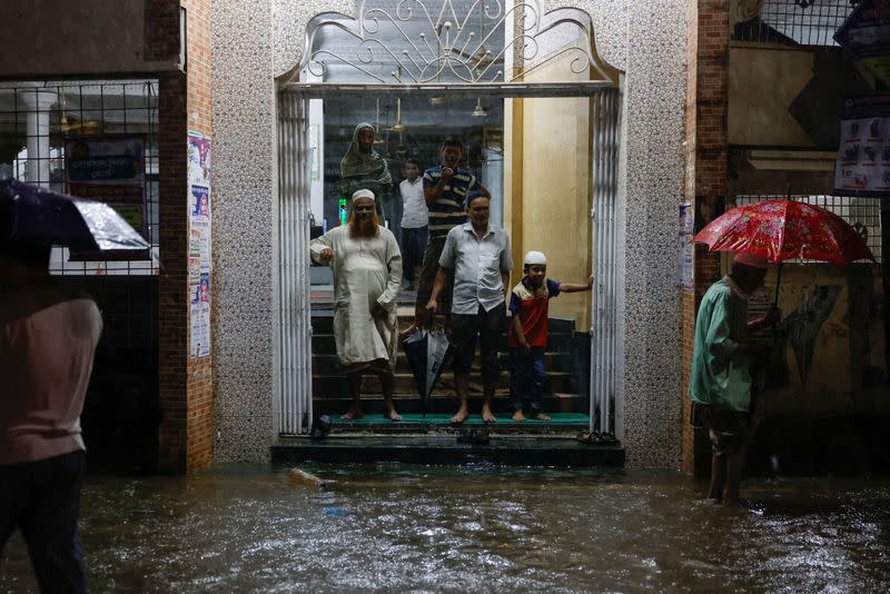 People wait on the gate of a mosque as streets are flooded before the Cyclone Sitrang hits in Dhaka