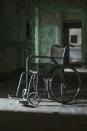 <p>A lone wheelchair sits in the middle of the hallway in an abandoned mental asylum. </p>