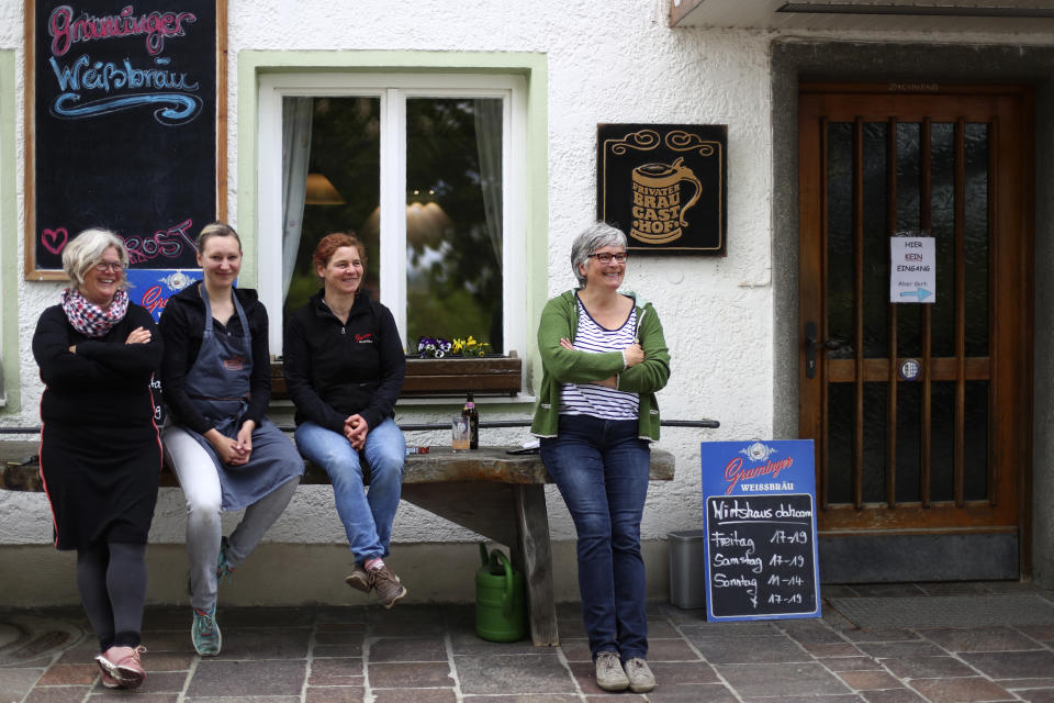 In this photo taken Friday, May 1, 2020 brewery daughters Birgit Detter, left, Iris Detter, second right, Sabine Detter, right, and waitress Elisabeth Haeckl rest in front of the 120 year old family brewery and traditional Bavarian restaurant in Altoetting, Germany. The 'Graminger Weissbraeu' brewery, which has been in the same family for a century, is preparing to welcome guests back to its restaurant for the first time in two months — with new rules and fears for the future. (AP Photo/Matthias Schrader)