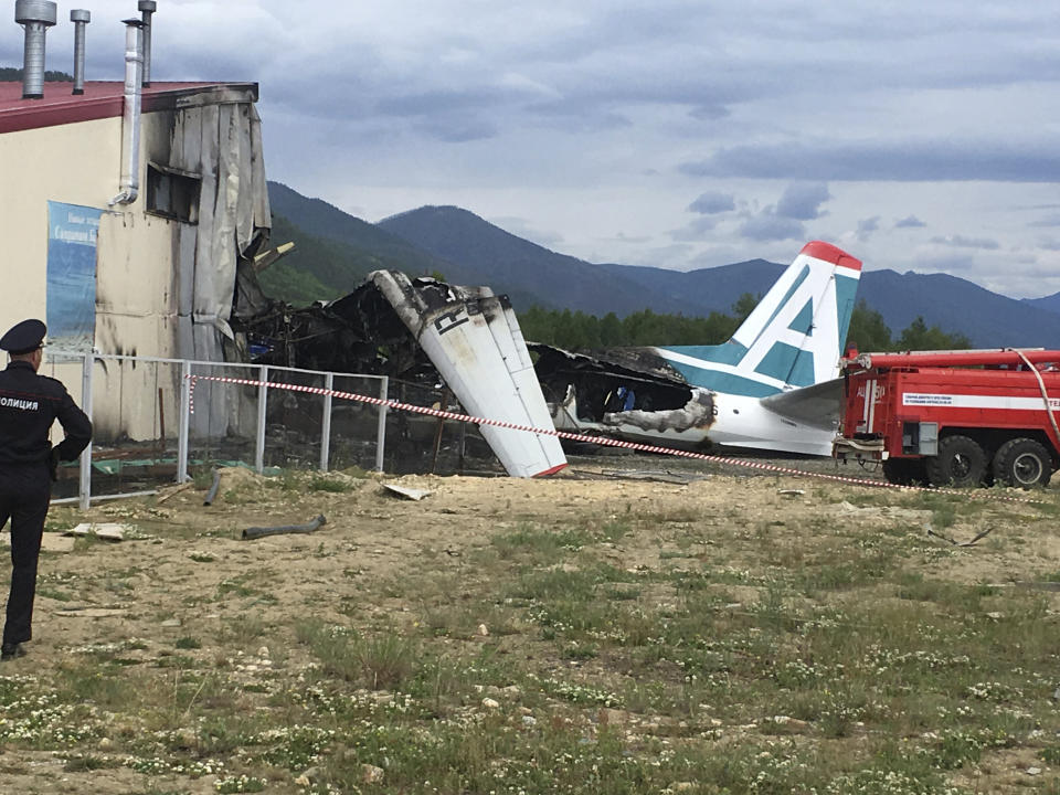 A police officer, left, looks at a part of plane An-24 after a crash during a landing in Nizhneangarsk, Republic of Buryatia, Russia, Thursday, June 27, 2019. According to the Russian Emergency Ministry, the two dead were members of the cabin crew. Forty-six passengers have been rescued, the ministry said. (AP Photo/Vladimir Dozmorov)