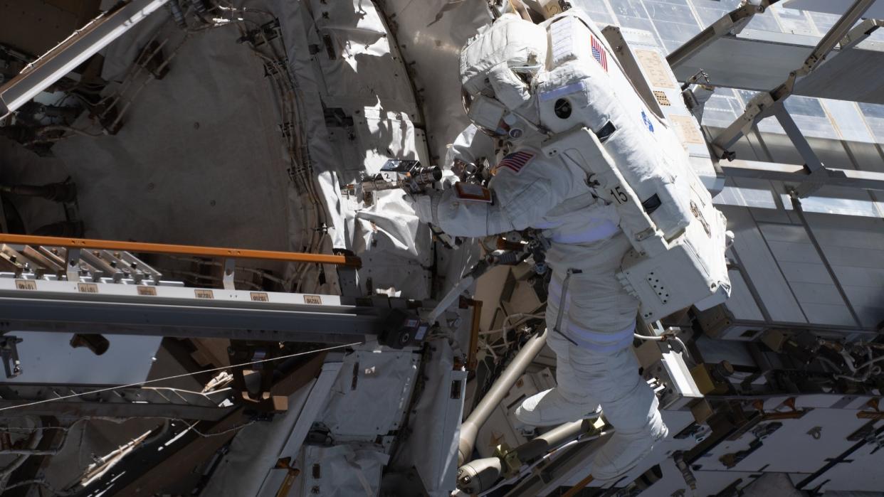  An astronaut in a spacesuit facing the international space station. 