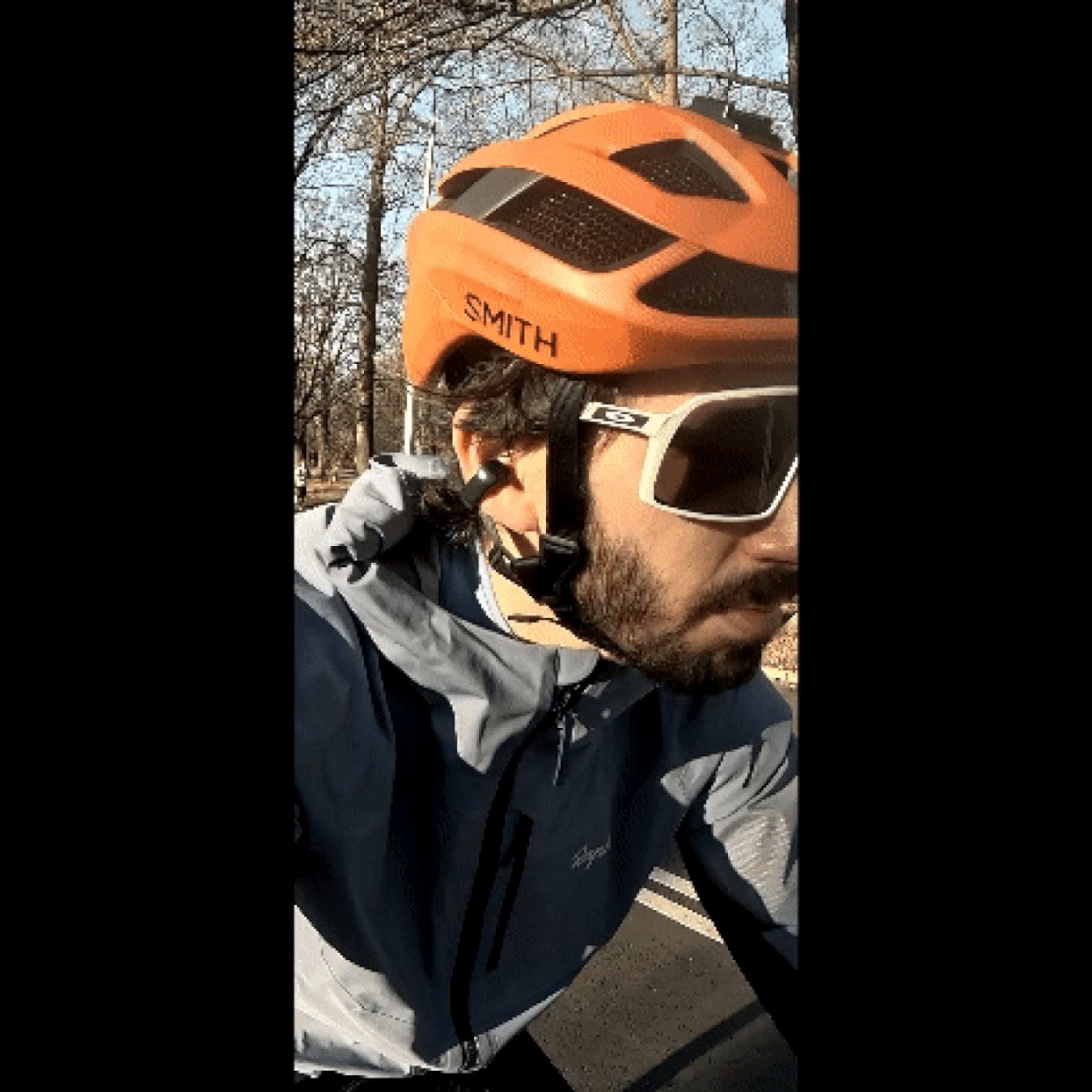 Close-up of the reporter biking in a park, wearing the Bose Ultra Open Earbuds, sunglasses, and a bike helmet. (Courtesy Harry Rabinowitz)
