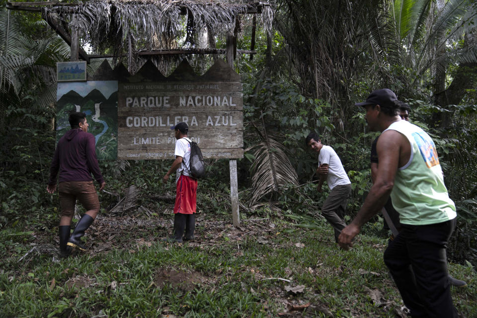 A group of men pass in front of a sign for the Cordillera Azul National Park in the Peru Amazon, Monday, Oct. 3, 2022. Residents in Kichwa Indigenous villages in Peru say they fell into poverty after the government turned their ancestral forest into a national park, restricted hunting and sold forest carbon credits to oil companies. (AP Photo/Martin Mejia)
