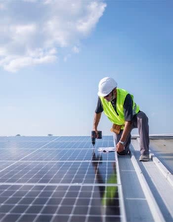 Man in a yellow safety vest installs solar panels on a roof.