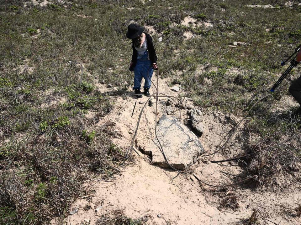 woman inspects large chunk of concrete entangled in rebar in a patch of dirt