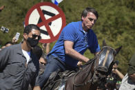 Brazil's President Jair Bolsonaro rides a horse greeting supporters outside the presidential palace in Brasilia, Brazil, Sunday, May 31, 2020. Bolsonaro mounted a horse from police that were guarding supporters of his government gathered outside the Planalto Palace. (AP Photo/Andre Borges)