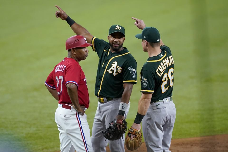 Texas Rangers third base coach Tony Beasley looks to the dugout as Oakland Athletics' Elvis Andrus, center, and Matt Chapman (26) talk about a ball hit by the Rangers' Eli White during the third inning of a baseball game in Arlington, Texas, Friday, July 9, 2021. (AP Photo/Tony Gutierrez)