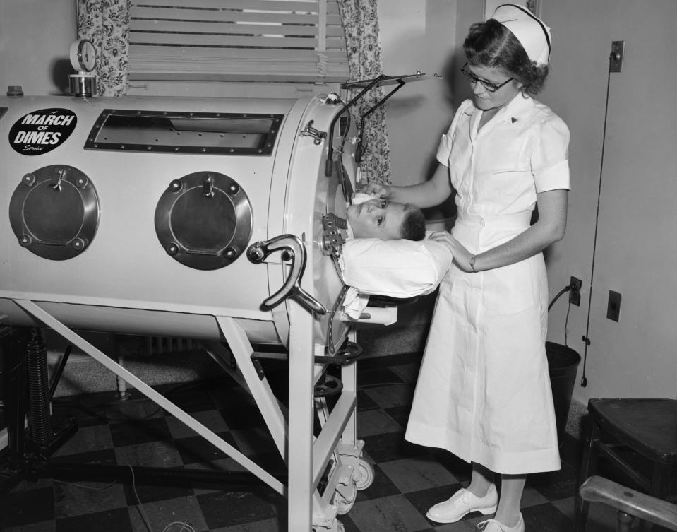 Nurse oversees boy in an iron lung.