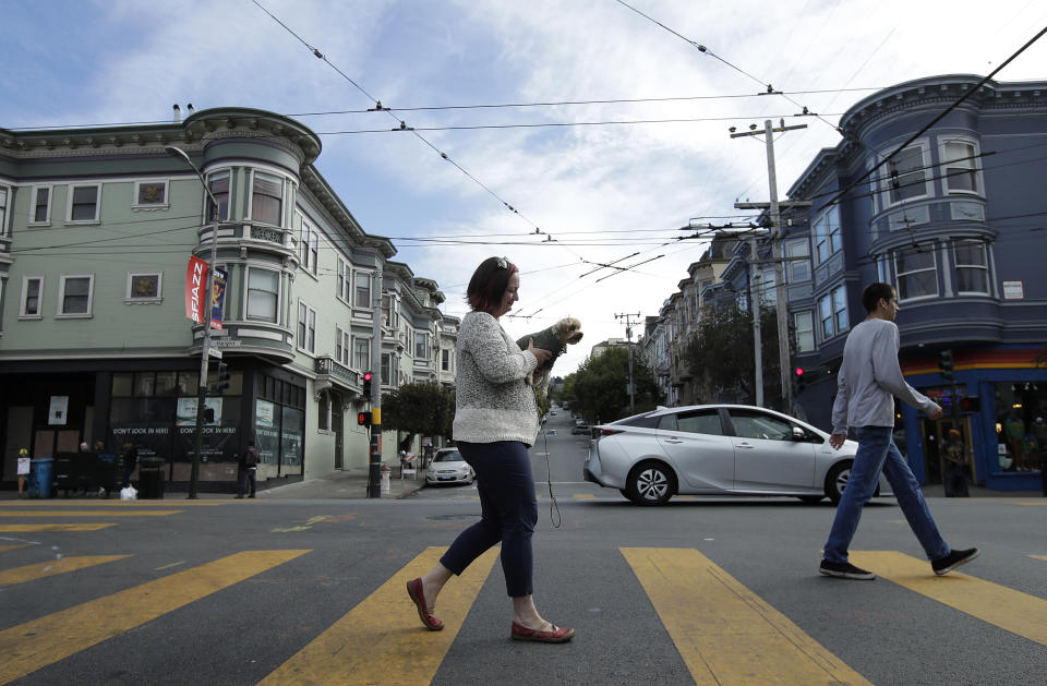 In this Oct. 1, 2018 photo, Christin Evans, owner of The Booksmith, carries her dog Joey Pistachio as she crosses Ashbury Street along Haight Street in San Francisco. A measure on San Francisco's Nov. 6 ballot would levy an extra tax on hundreds of the city's wealthiest companies to raise $300 million for homelessness and mental health services. It's the latest battle between big business and social services advocates who say that companies such as Amazon, Google and Salesforce can afford to help solve severe inequities caused by business success. (AP Photo/Jeff Chiu)