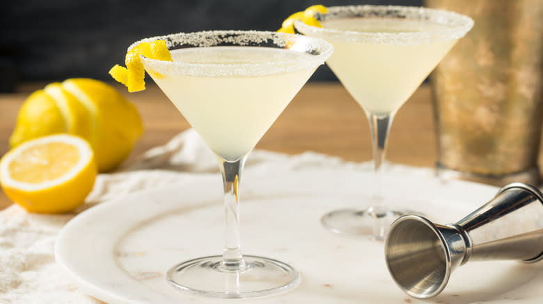 Two lemon drop martinis with a jigger and sliced lemons