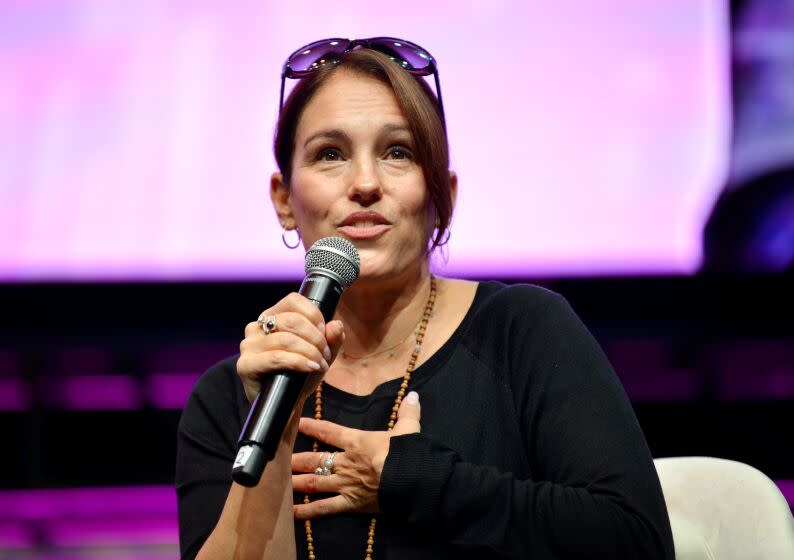 Amy Jo Johnson speaks during the "Mighty Morphin Power Rangers" panel, she's wearing a black top and holds a mic.