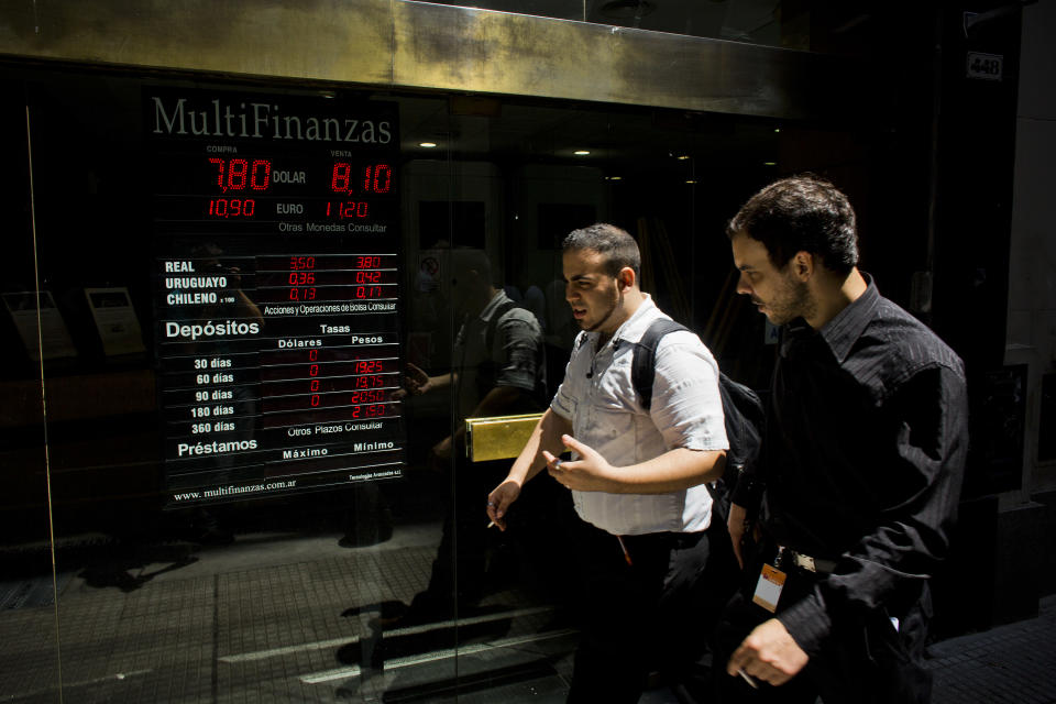 People walk by a sign indicating the exchange rate between the Argentine peso and the U.S. dollar in Buenos Aires, Argentina, Thursday, Jan. 23, 2014. Argentina's peso has plunged just over 17 percent in the last two days against the U.S. dollar, and economic analysts expect inflation to hit 30 percent this year. (AP Photo/Victor R. Caivano)