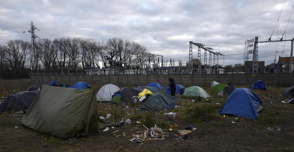 In this photo taken on Tuesday Jan. 15, 2019 A migrant walks through tents in a makeshift camp in Calais, northern France. Land, sea and air patrols are combing the beaches, dunes and frigid, murky coastal waters of northern France, the gateway to Britain, in a bid to stop migrants, mostly Iranian, from an ever more risky tactic to sneak across the English Channel _ in small boats and rubber rafts. (AP Photo/Michel Spingler)