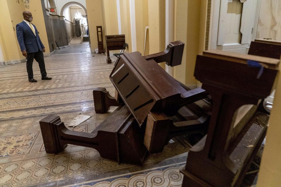 A senator looks at toppled furniture in a marble hallway.