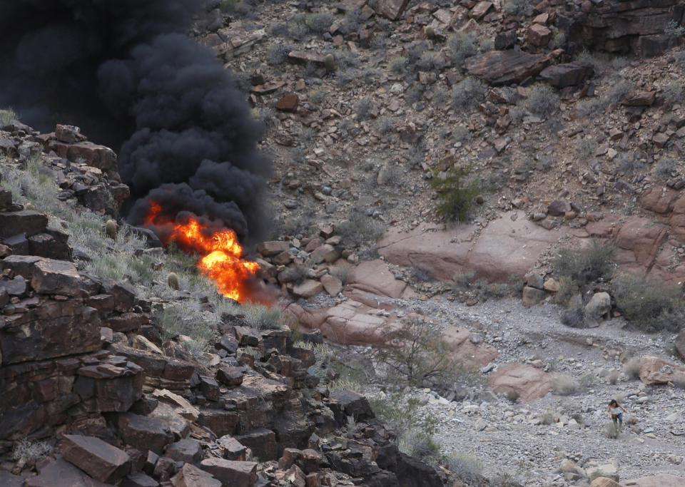 FILE - In this Saturday, Feb. 10, 2018, file photo, a survivor, lower right, walks away from the scene of a deadly tour helicopter crash along the jagged rocks of the Grand Canyon in Arizona. The pilot of the helicopter that crashed in the Grand Canyon in 2018, killing five British tourists, says he lost control of the aircraft after a "violent gust of wind" sent it spinning. The National Transportation Safety Board released its final report Thursday, Jan. 14, 2021, that said tailwinds, potential downdrafts and turbulence were the probable cause of the loss of control and tail-rotor effectiveness. (Teddy Fujimoto via AP, File)