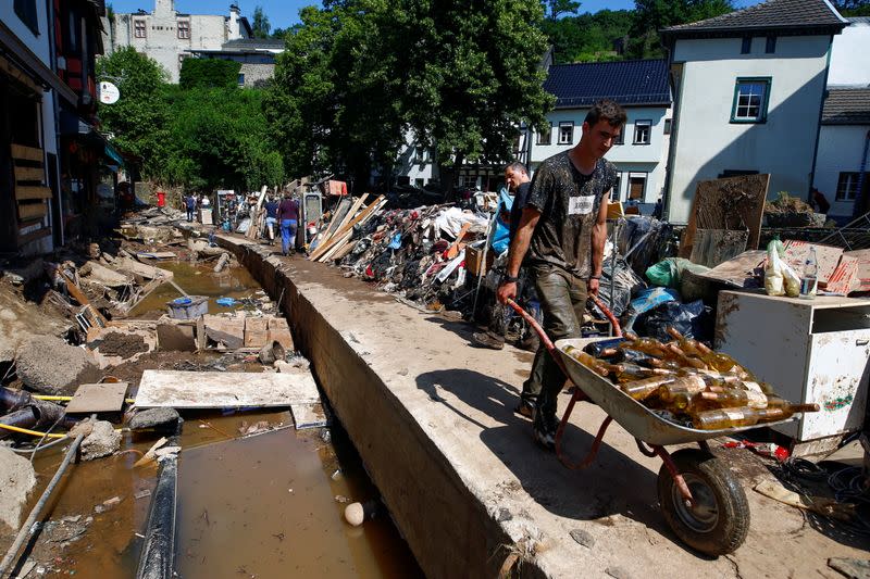 Un hombre transporta botellas de vidrio en una carretilla junto a los escombros depositados a lo largo de una calle en una zona afectada por las inundaciones causadas por las fuertes lluvias en Bad Muenstereifel, Alemania