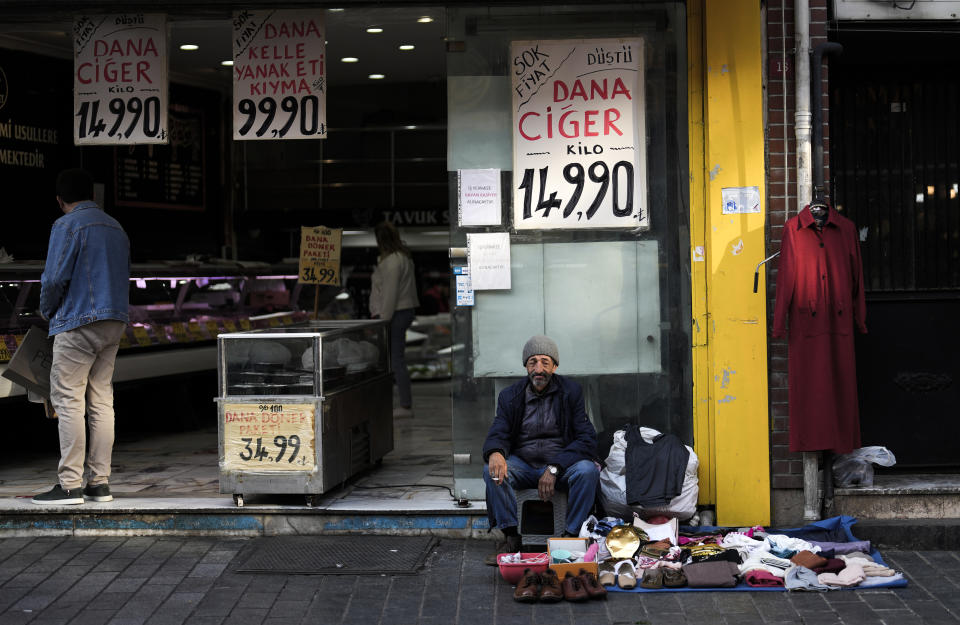 An elderly street vendor displays clothes for sale next to a meat shop in an outdoor market in Fatih district of Istanbul, Turkey, Tuesday, May 23, 2023. Two opposing visions for Turkey’s future are on the ballot when voters return to the polls Sunday for a runoff presidential election, which will decide between an increasingly authoritarian incumbent President Recep Tayyip Erdogan and challenger Kemal Kilicdaroglu, who has pledged to restore democracy. (AP Photo/Khalil Hamra)