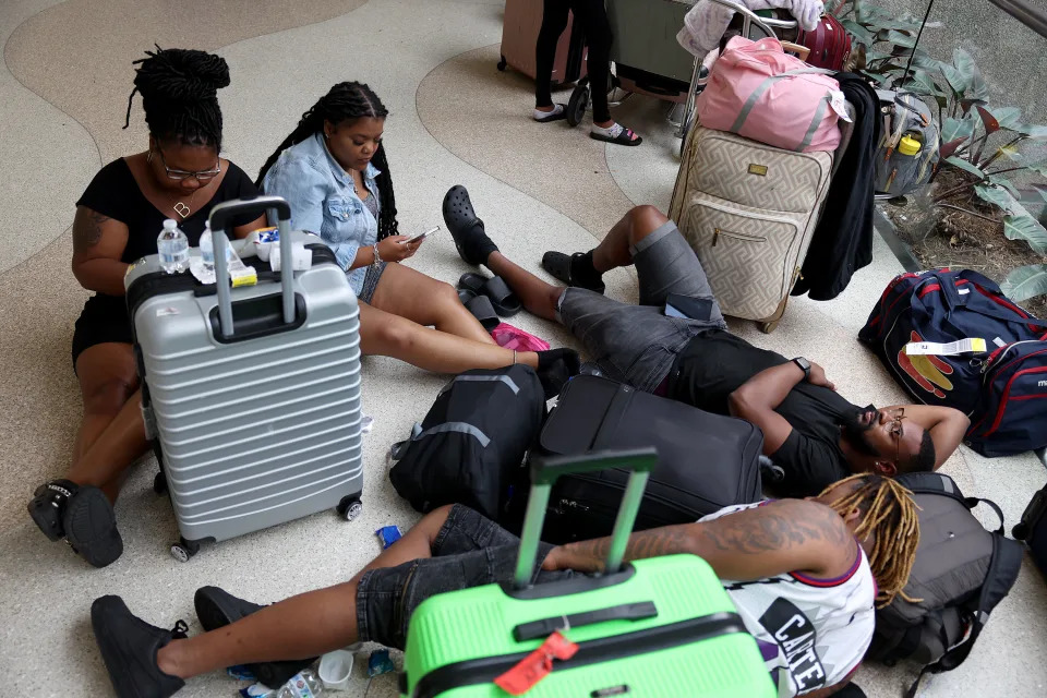 People sitting and lying on an airport floor with their luggage