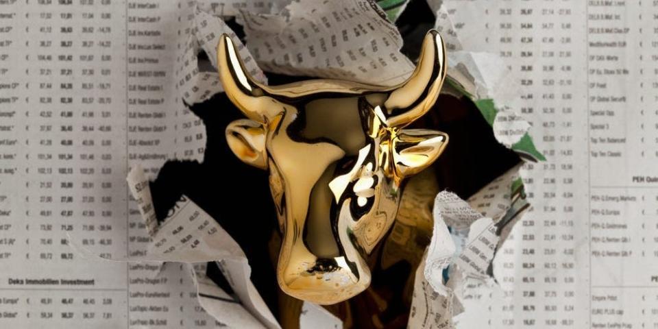 Gold bull emerging through newspaper