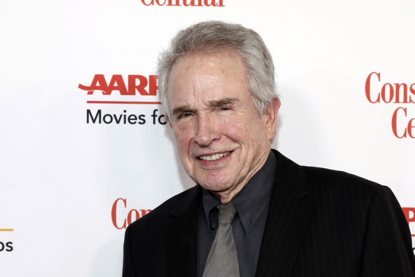 An old man with white hair smiles in a dark suit