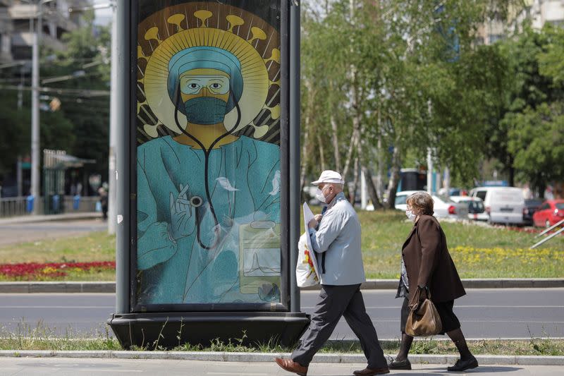 People pass by an outdoor poster that shows a medic depicted in a similar manner as Jesus Christ would be portrayed by Christian Orthodox religious paintings