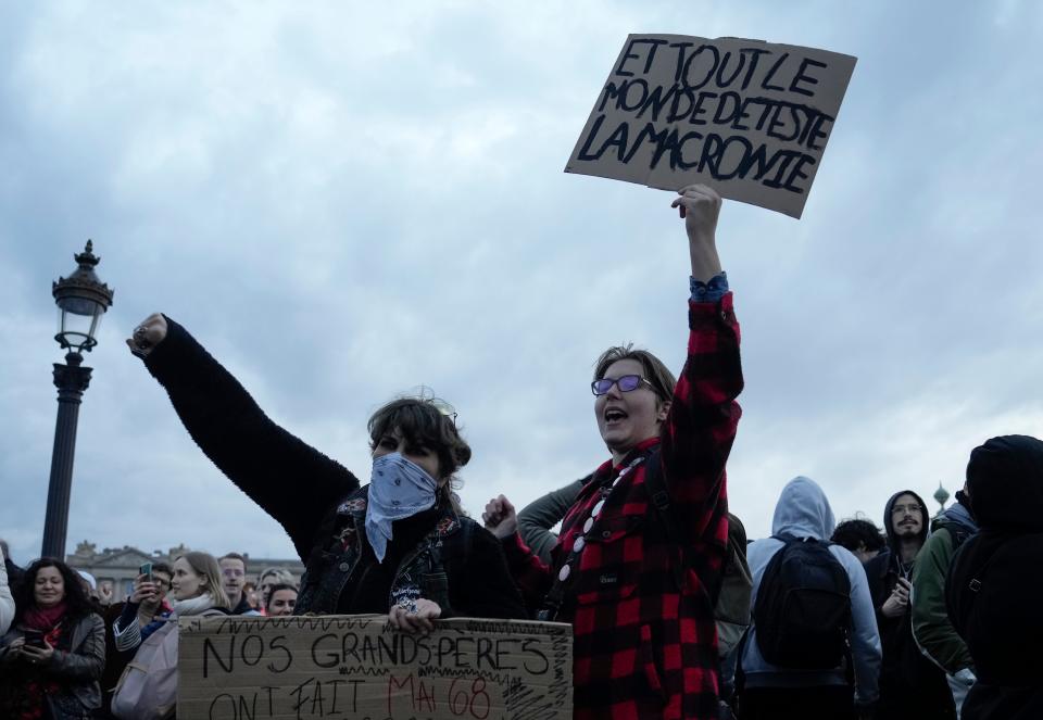 A woman holds a placard that reads, "all heat the Macronie", referring to French President Emmanuel Macron during a protest in Paris, Friday, March 17, 2023.