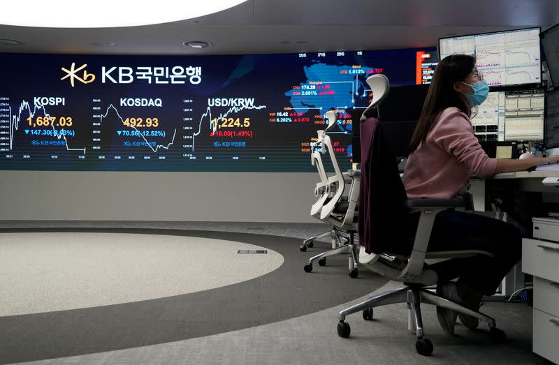 A currency dealer works in front of an electronic board showing the Korea Composite Stock Price Index (KOSPI) at a dealing room of a bank in Seoul