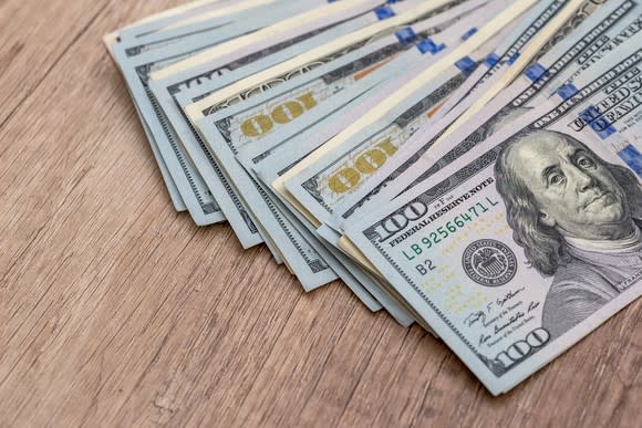 A stack of U.S. hundred dollar bills spread out on a wooden surface.