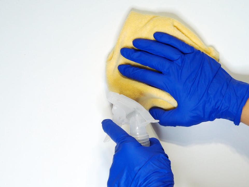 Person wearing blue gloves cleans the white surface of a cabinet or wall with a white vinegar. 